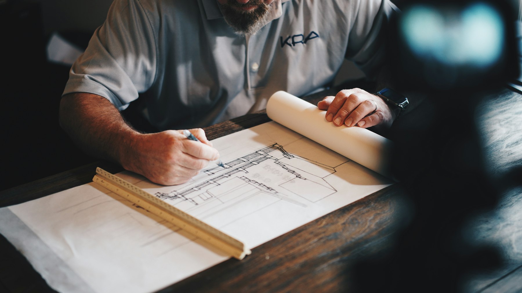 Main dessinant un plan d’architecture sur une table en bois